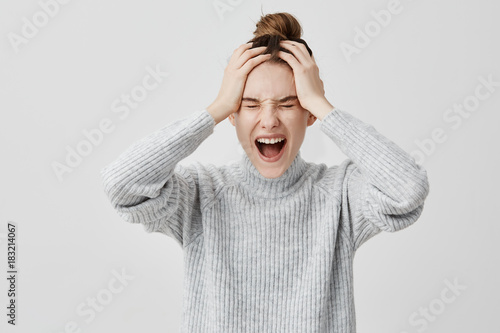 Headshot of frustrated female 30s screaming grabbing her head. Perplexed businesswoman being in shock shouting in despair having problem with work.  Emotions concept photo