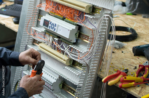 Hands of electrical technician assembling low voltage industrial HVAC control cubicle in workshop. Close-up photo.