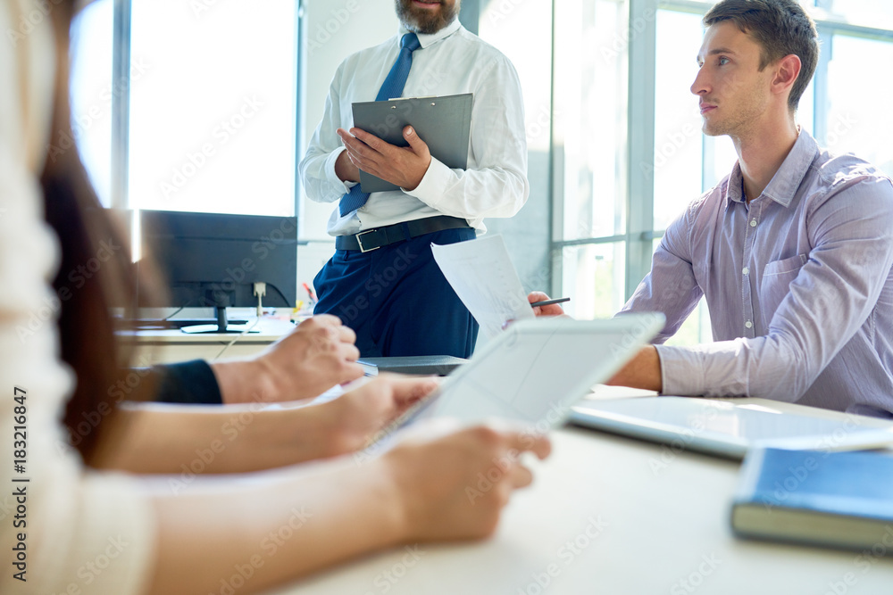 Obraz premium Mid-section view of business people sitting at meeting table in modern office listening to boss during morning briefing