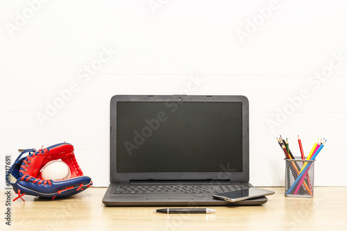 Canvas Print Laptop on wooden table with baseball glove and ball, pen, colored pencils and smart phone Working space in loft