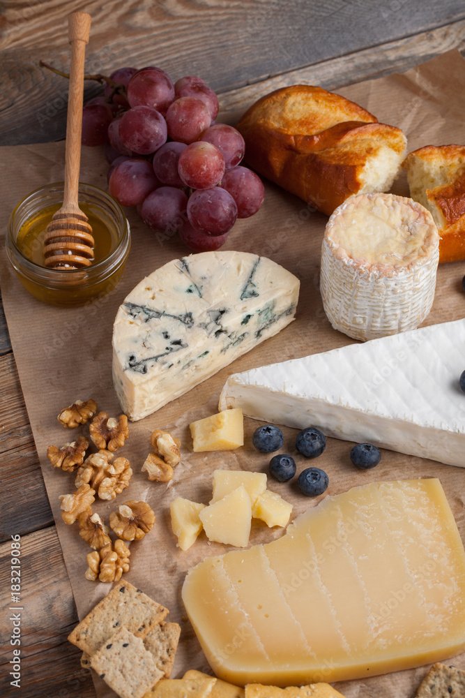 Fototapeta premium Tasting cheese dish on a wooden plate. Food for wine and romantic, cheese delicatessen on a wooden rustic table. Top view
