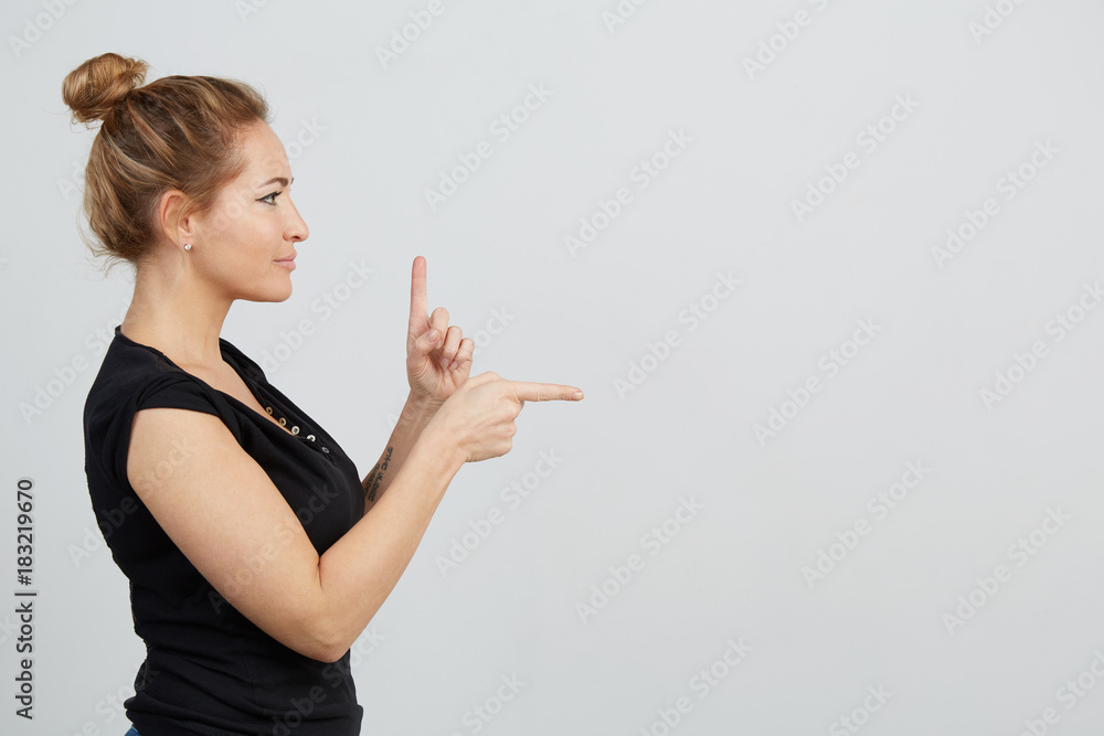 Emotional beautiful young adult woman portrait. Studio shoot. Isolated on White Background. A woman in a black T-shirt is standing by the profile. The index fingers of her hands point upwards and Emotional beautiful young adult woman portrait. Studio shoot. Isolated on White Background. A woman in a black T-shirt is standing by the profile. The index fingers of her hands point upwards and
