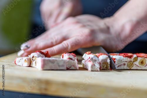Female Hands Cutting Strawberry Fruit and Nut Nougat with Knife on Wooden Board