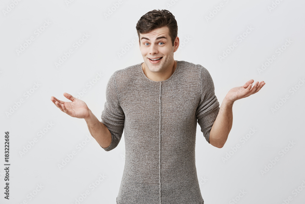 Confused caucasian man with trendy hairdo in sweater, shrugs shoulders, keeps palms open in bewilderment as makes difficult choice in his life, not knows what to do. Life perception and attitude. Confused caucasian man with trendy hairdo in sweater, shrugs shoulders, keeps palms open in bewilderment as makes difficult choice in his life, not knows what to do. Life perception and attitude.