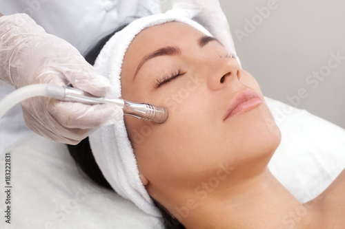 The cosmetologist makes the procedure Microdermabrasion of the facial skin of a beautiful, young woman in a beauty salon.Cosmetology and professional skin care.