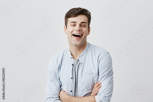 Cheerful young european smiling broadly with teeth, rejoicing at positive news or promotion at work,keeping arms folded. Human emotions, feelings, attitude and reaction © Cookie Studio