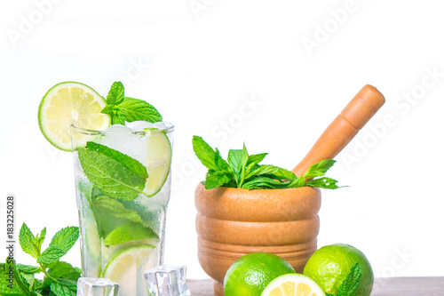 Mojito cocktail with ingredients. Fresh lime, mint leaves and ice cubes, morter with mint and brown sugar on a wooden background. Refreshing alcohol drink. Isolated on white background.. photo