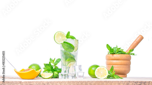 Mojito cocktail with ingredients. Fresh lime, mint leaves and ice cubes, morter with mint and brown sugar on a wooden background. Refreshing alcohol drink. Isolated on white background..