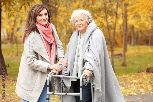 Senior woman with walking frame and young caregiver in park