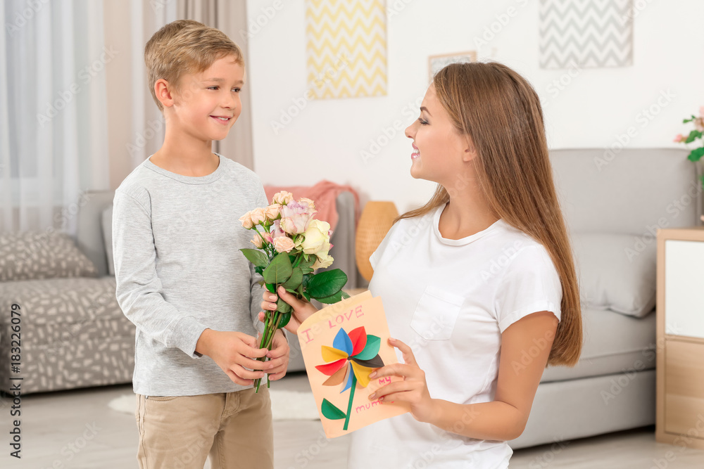 Young woman receiving flowers and card from her little son on Mother's Day at home Young woman receiving flowers and card from her little son on Mother's Day at home