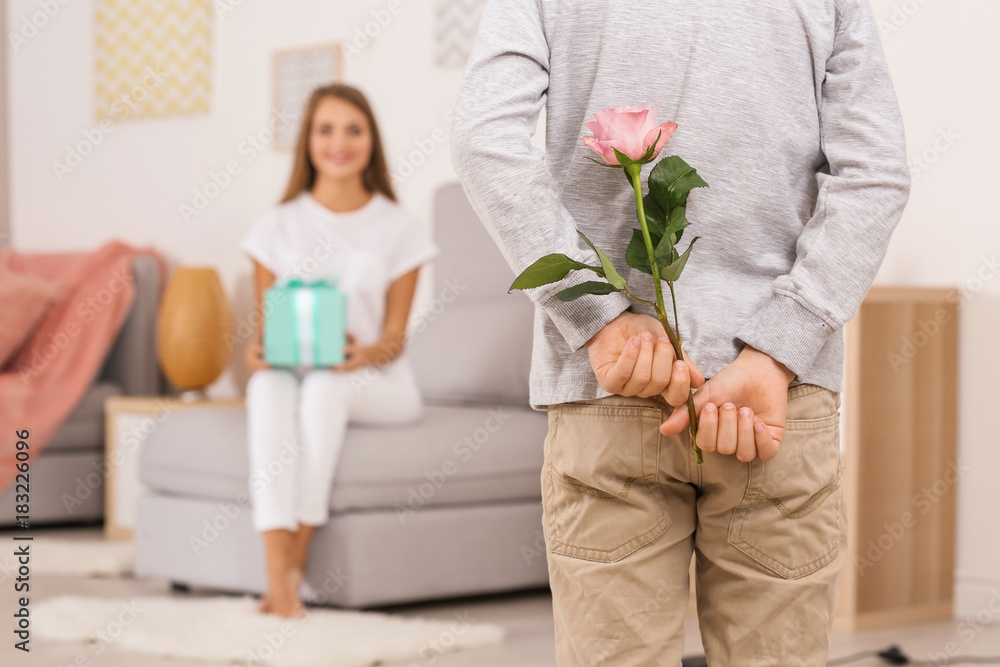 Cute little boy hiding flower for mother behind his back at home Cute little boy hiding flower for mother behind his back at home