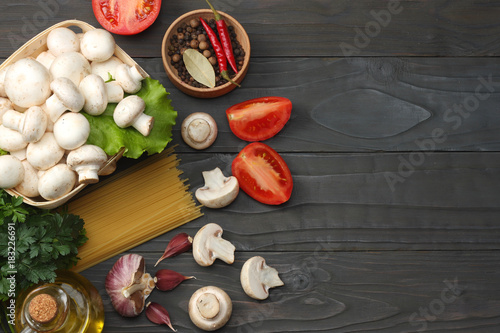 Italian food background, with tomatoes, parsley, spaghetti, mushrooms, oil, lemon, peppercorns on dark wooden table. Top view