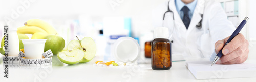 Nutritionist doctor writes the medical prescription for a correct diet on a desk with fruits, drugs and supplements, web banner and copy space template