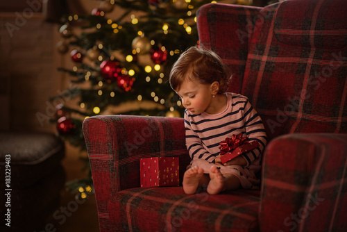 happy little girl sitting near a chrismas tree laughing waiting for presents  © Lumistudio