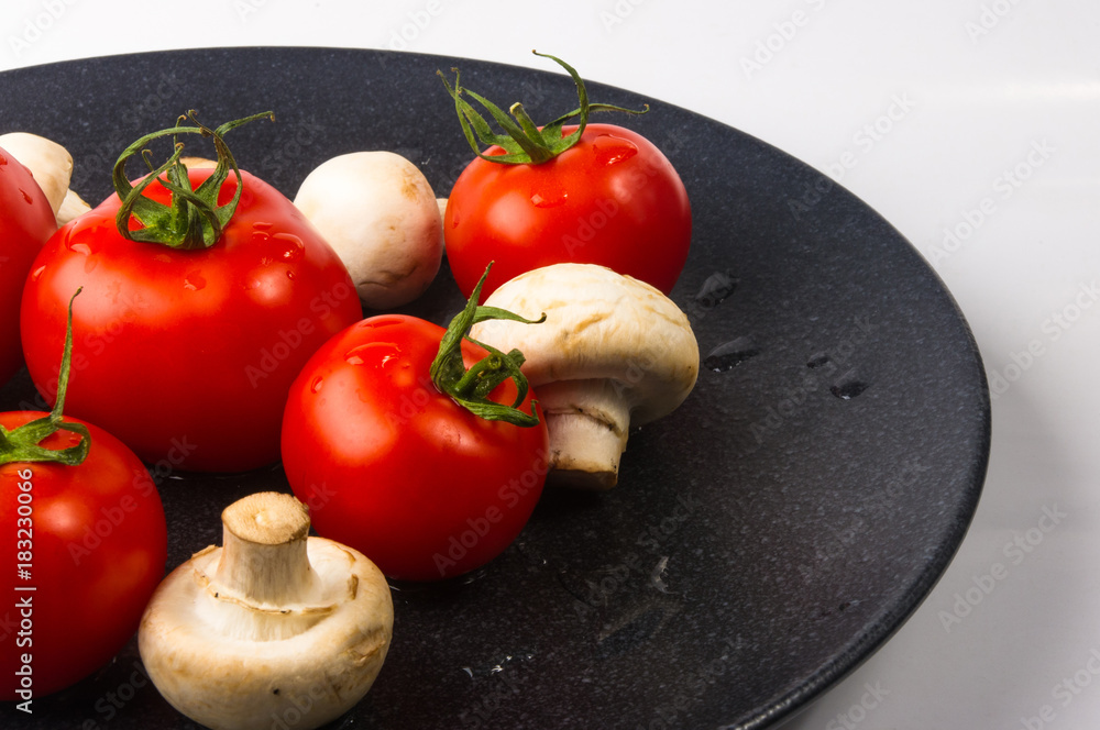 fresh tomatoes and mushrooms - champignons on black plate fresh tomatoes and mushrooms - champignons on black plate