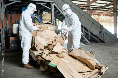 Fotografie Portrait of two factory workers wearing biohazard suits sorting reusable cardboa