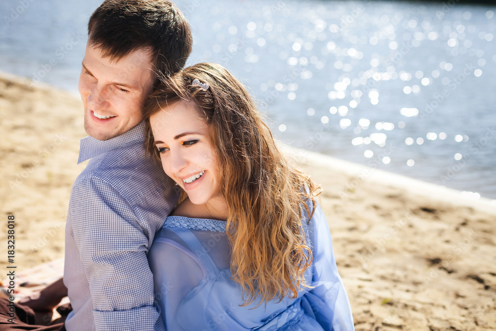 Obraz premium young lovely couple resting on beach, handsome boyfriend and beautiful girlfriend smiling and sitting back to back on coast river, happy family concept