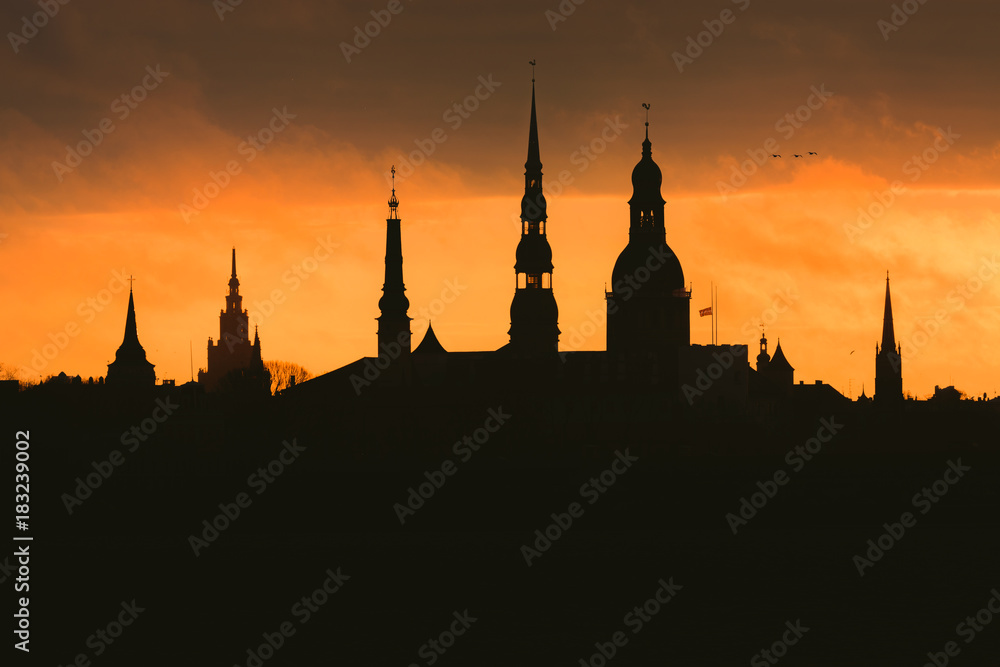 City silhouette of Riga, Latvia in colorful morning sunset. Church towers and popular landmarks in background with stunning yellow sky. 