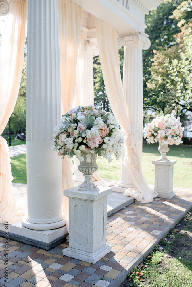 White wedding arch with big peach bouquets on the white stands