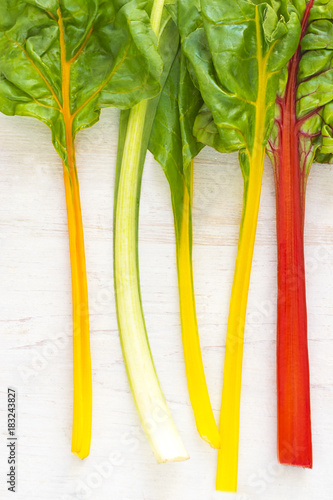 Close-up of multicolored fresh beet leaves on a white wooden background. Ingredients of new  vegetarian cuisine