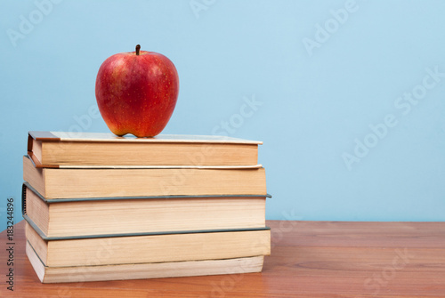 Red apple and books on a wooden table and blue background and free space for text