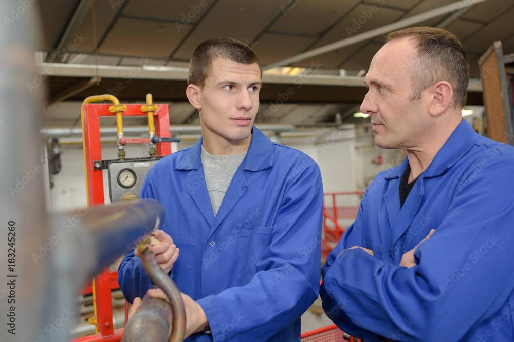 Men stood by machinery in factory Men stood by machinery in factory