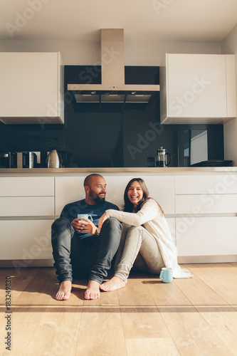 Couple sitting on kitchen floor and having coffee