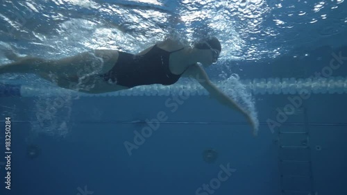 Female swimmer swims crawl stroke on swimming path in transparent water pool photo