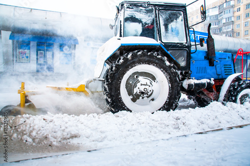 A blue tractor clears snow on the road