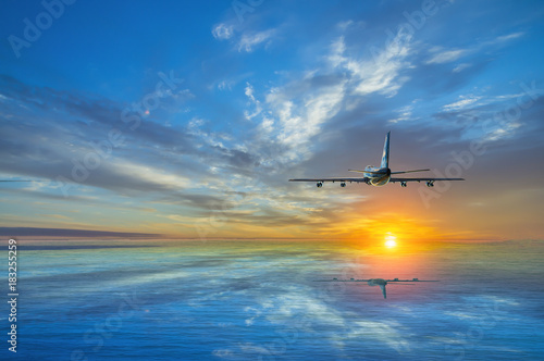 The airplane climbs, flying over the sea towards the sun at sunset