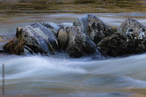 Lichen covered rock formation surrounded by swiftly running waters, horizontal aspect