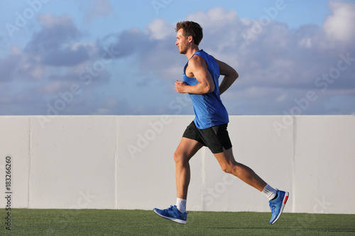 Young man runner running in city park on summer grass outdoors at sunset at outdoor stadium fitness centre. Healthy lifestyle.