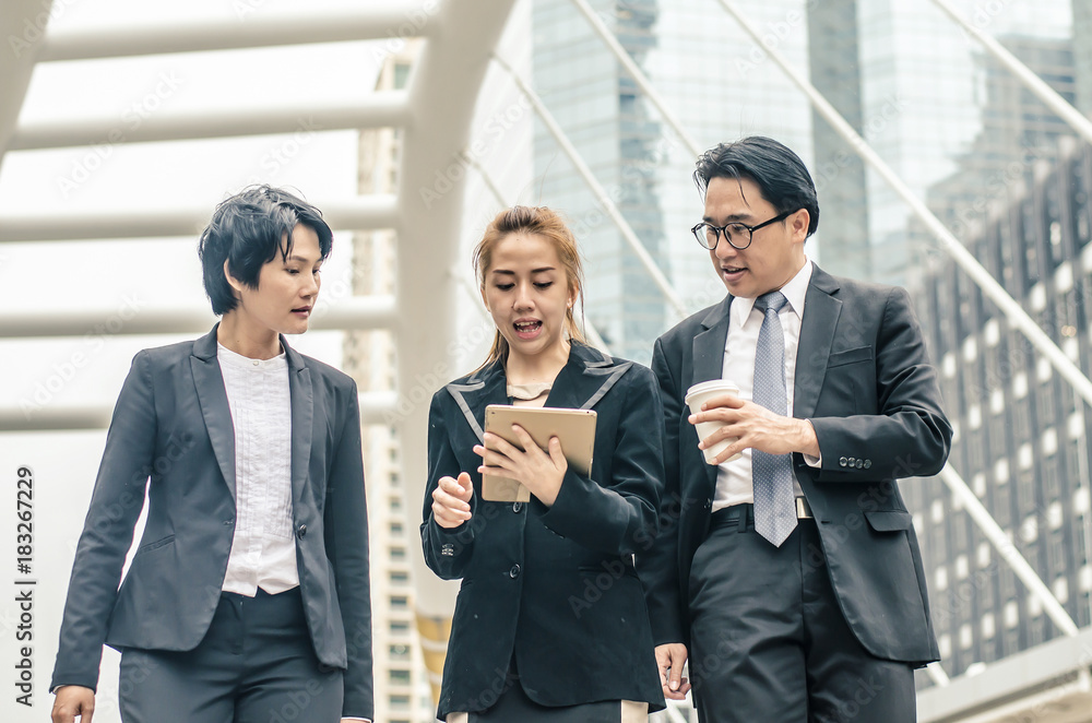 young businessmen and two lady in classic suits are holding cups of coffee, talking and smiling, standing outside the office building. young businessmen and two lady in classic suits are holding cups of coffee, talking and smiling, standing outside the office building.