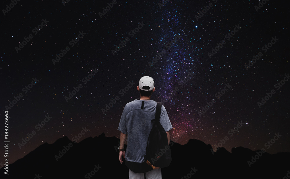 Fototapeta premium a man with backpack standing alone with colorful stars on night sky background