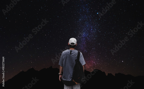 a man with backpack standing alone with colorful stars on night sky background