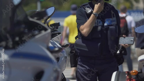 Female police officer standing next to motorbike, checking mobile phone on duty