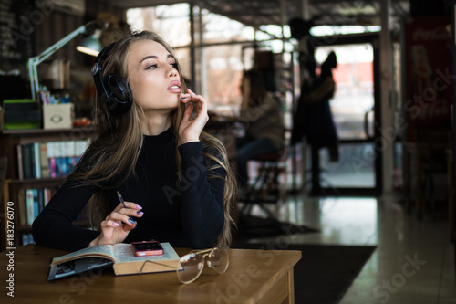 Portrait of beautiful female student listen or studying on-line training course in headphones, charming young woman have breakfast in coffee shop.