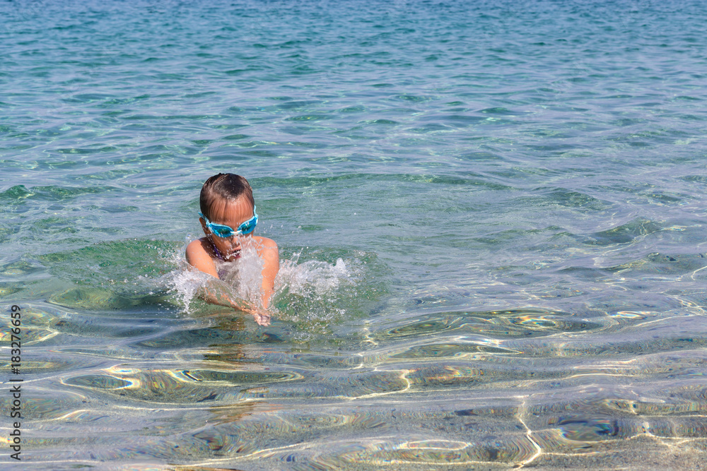 Young tourist girl in swimming sports glasses is floating in the Aegean Sea on the coast of Sithonia Peninsula