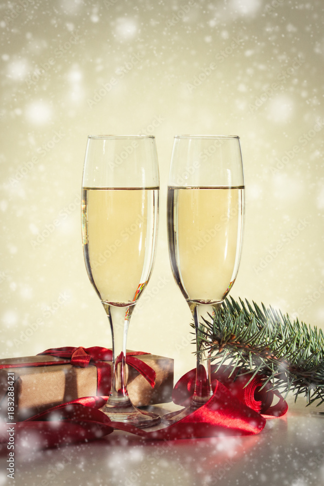 The concept of Christmas. Two glasses with champagne, a gift and a fur-tree branch. Snowfall The concept of Christmas. Two glasses with champagne, a gift and a fur-tree branch. Snowfall