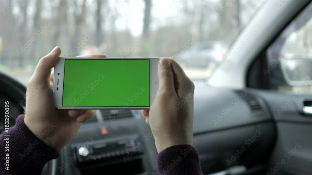 A hand holding a smartphone with green blank screen in the car for direction, massage, location, business. Man sits in modern car and works on smartphone - green screen - closeup. Chroma key. A hand holding a smartphone with green blank screen in the car for direction, massage, location, business. Man sits in modern car and works on smartphone - green screen - closeup. Chroma key.