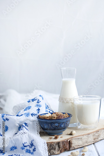 Milk in a glass and in a bottle  muesli in a blue cup. on white wooden background and tablecloth with blue flowers