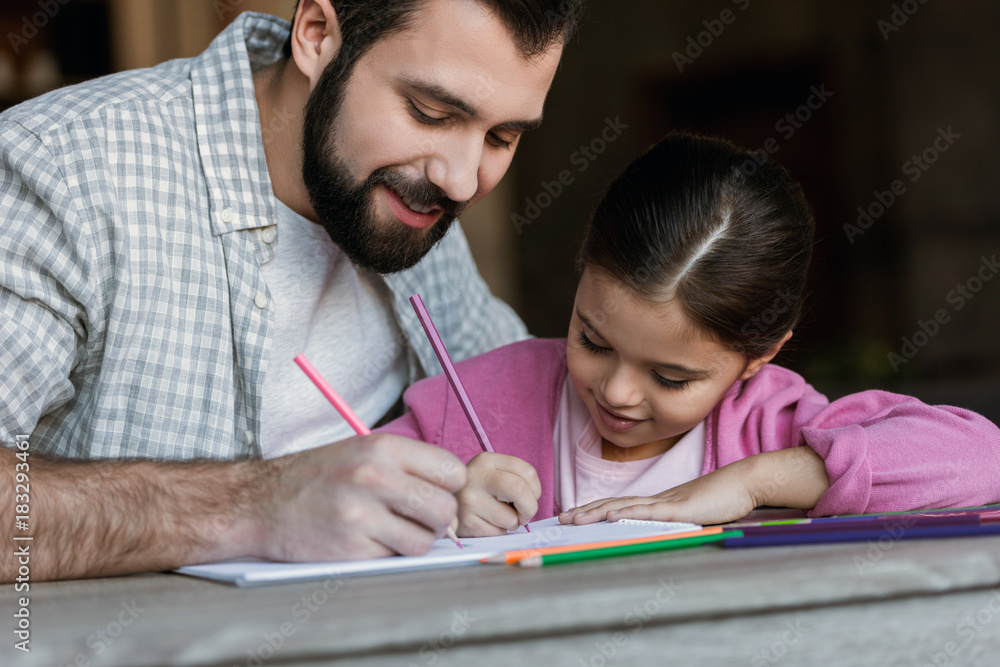 happy father with little daughter sitting at table and drawing in scrapbook at home