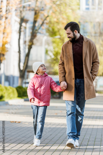 cheerful father with little daughter walking outside in autumn outfit and looking at each other. outside