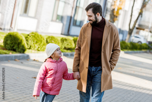 cheerful father with little daughter walking outside in autumn outfit and looking at each other. outside