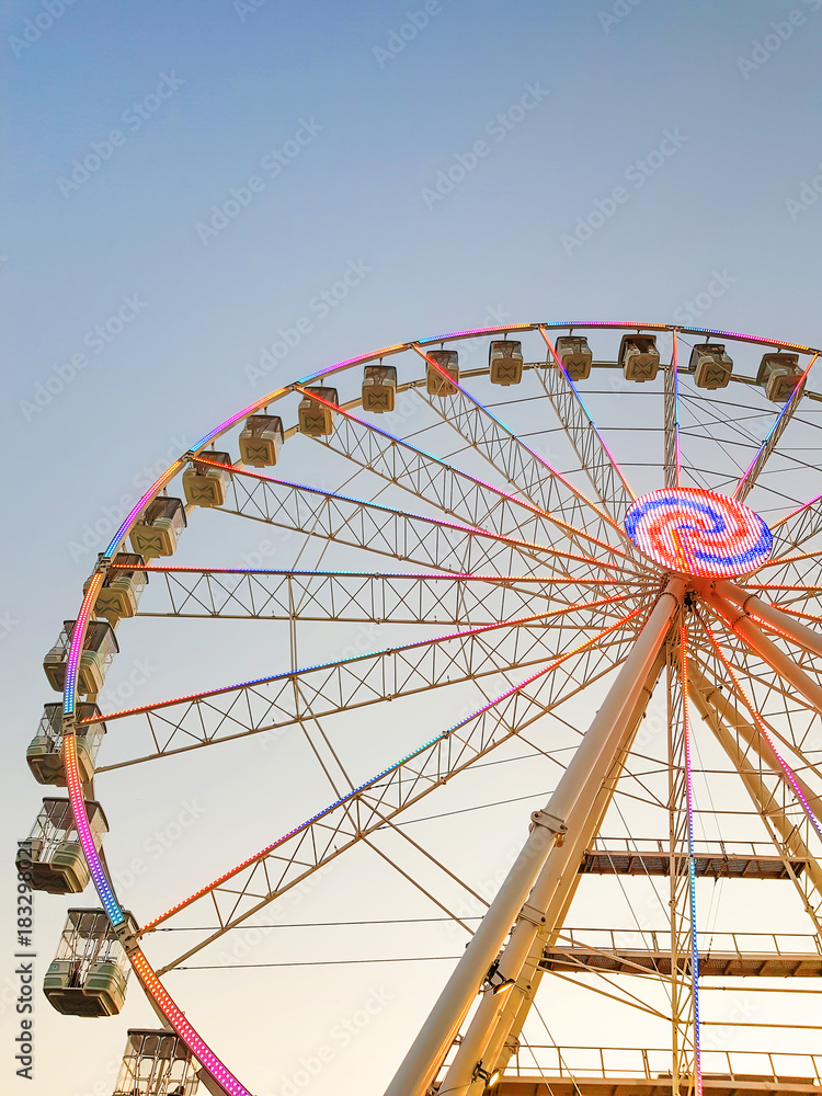Part of ferris wheel against a blue sky background with colorful lights.