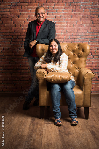 portrait of senior indian couple while sitting on sofa of wing chair
