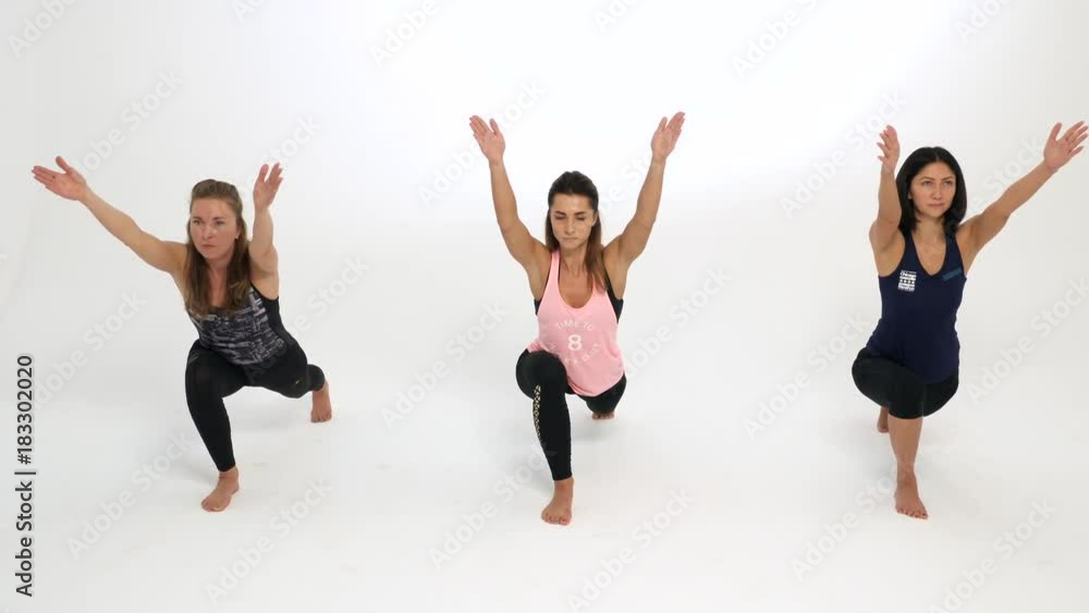 Group of women demonstrates a yoga pose against a white background. They are showing a warrior pose. Group of women demonstrates a yoga pose against a white background. They are showing a warrior pose.