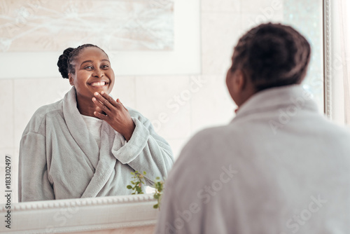 Smiling African woman looking in her bathroom mirror