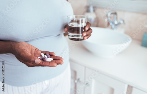 African woman holding pills and a glass of water