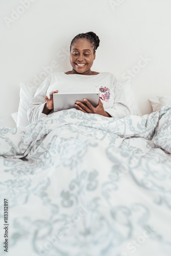 Smiling African woman using a digital tablet in bed